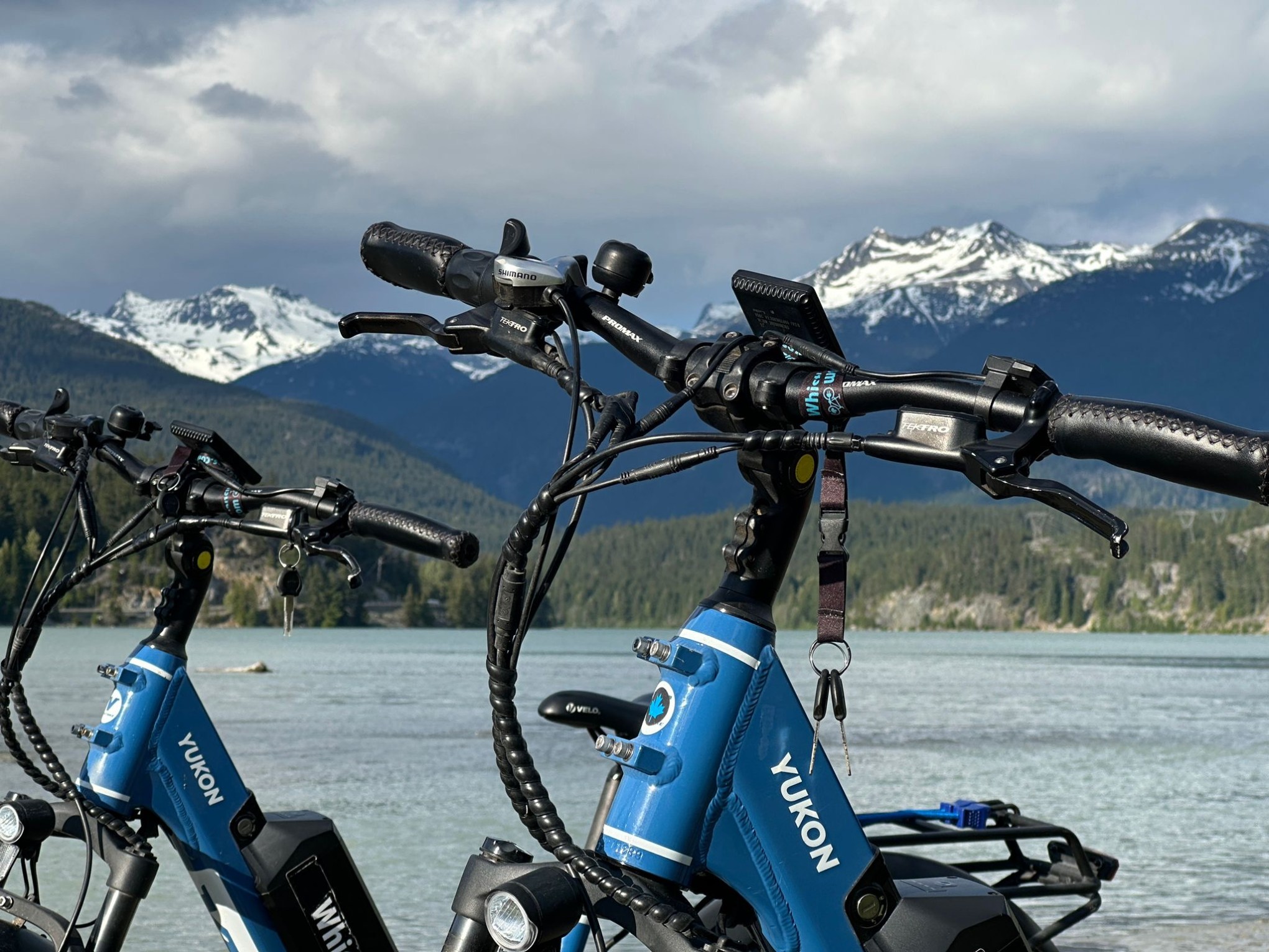 Blue electric bikes near a lake with snowy mountains in the background.