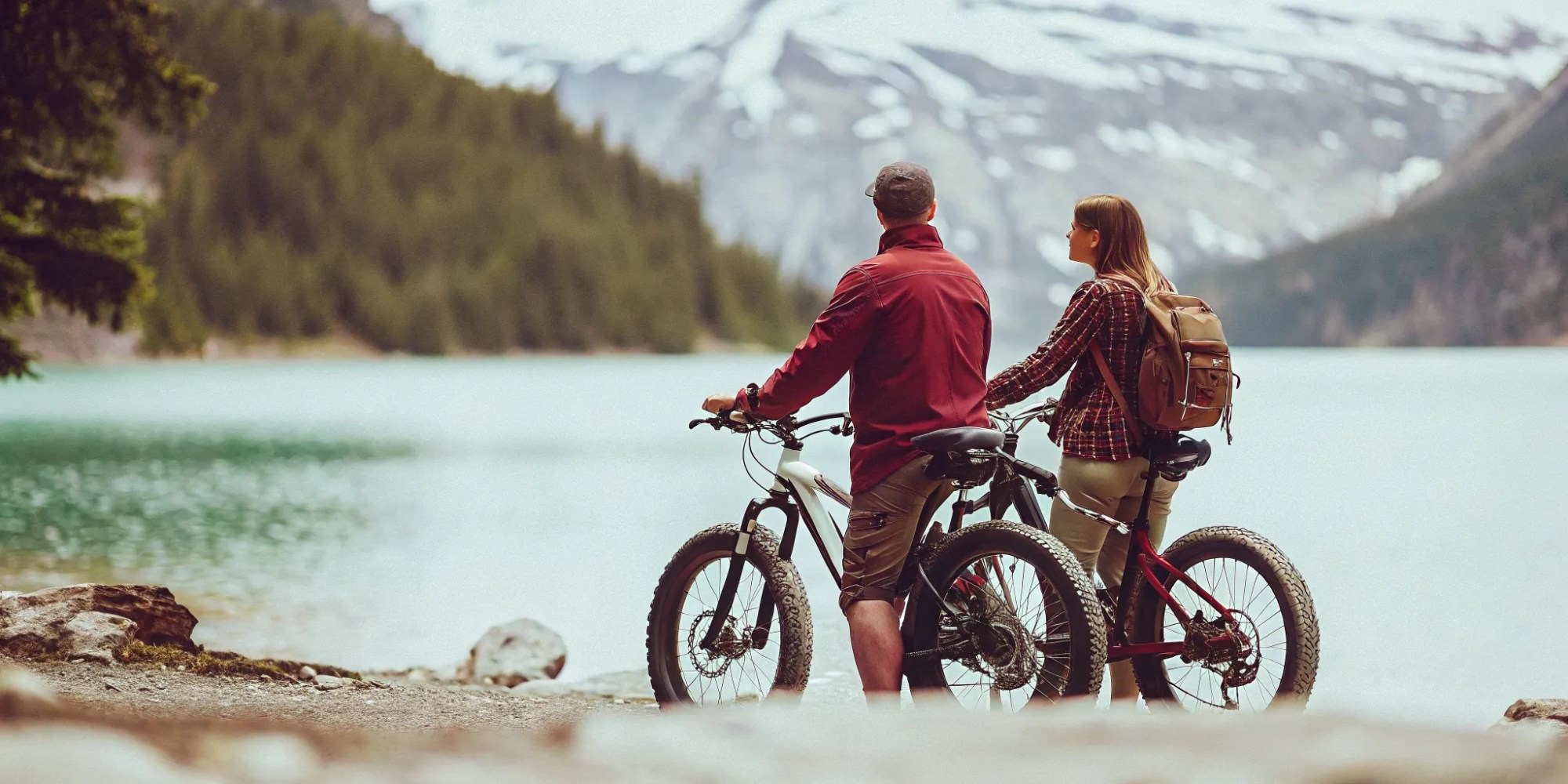 Fat tire e-bikes beside a turquoise glacier-fed alpine lake in Whistler BC with snow-capped Coast Mountains and cedar forest