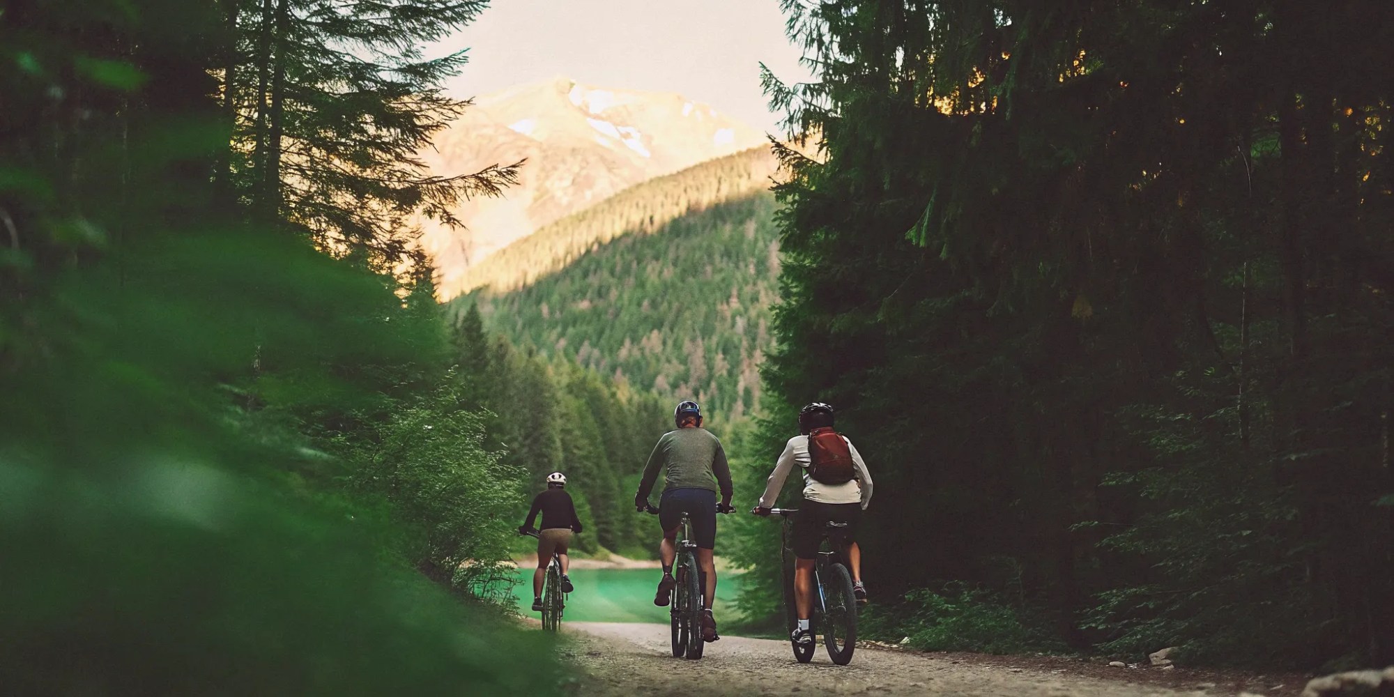 Group of riders on fat tire electric bikes on a forested valley trail in Whistler with golden October sunlight, autumn foliage, and turquoise lake visible through trees
