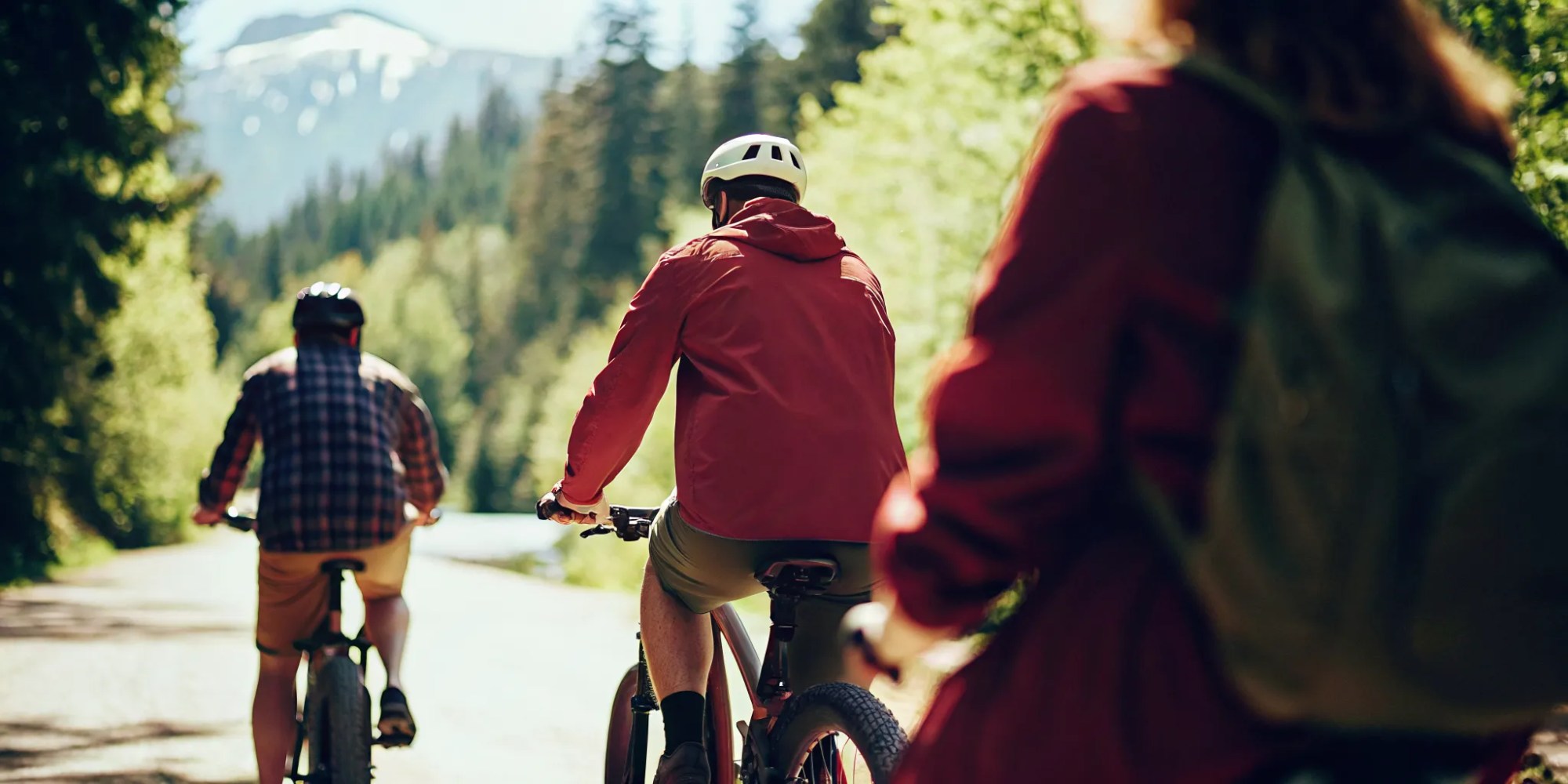 Group of cyclists on fat tire electric bikes riding a paved trail alongside an alpine lake in Whistler with mountains in the background